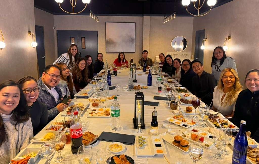 Filipino nurses enjoying a communal dinner with Towne Kids in a modern, warmly lit venue.